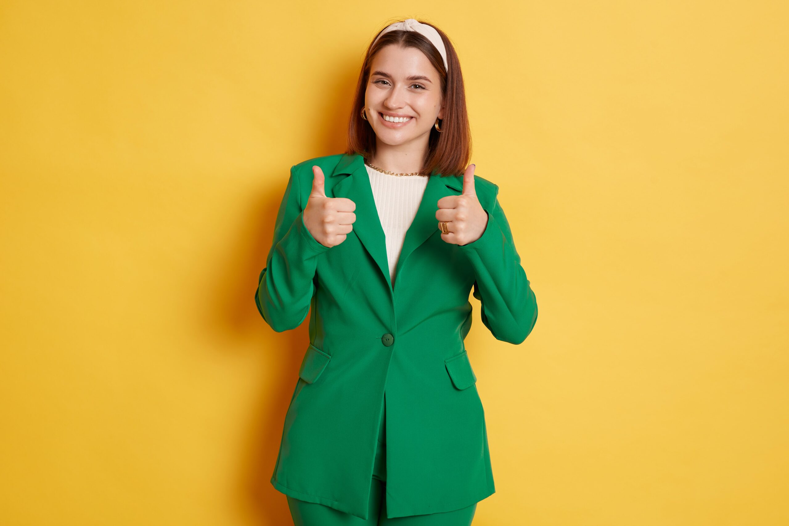 attractive-woman-wearing-green-jacket-standing-isolated-yellow-background-showing-like-gesture-thumb-ups-recommend-approved-sign-min